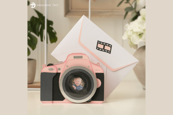 Pink camera-shaped fun fold card with a photo in the lens, next to an envelope, suitable for Cricut projects.