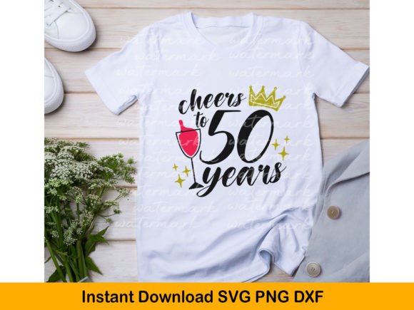 White t-shirt featuring 'cheers to 50 years' design with wine glass and gold crown, laid on a wooden surface.