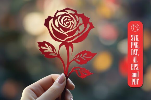 Hand holding a red rose cutout with intricate petal and leaf details, blurred background.