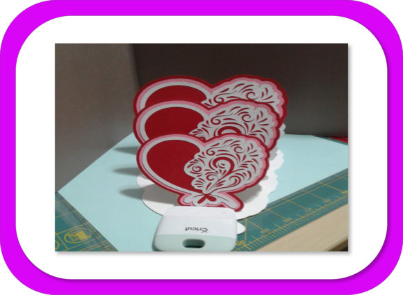 Triple easel card with layered hearts and floral patterns, standing on a crafting mat.