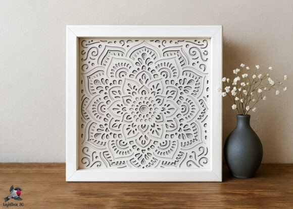 White mandala flower shadow box with detailed layered patterns on a wooden table.