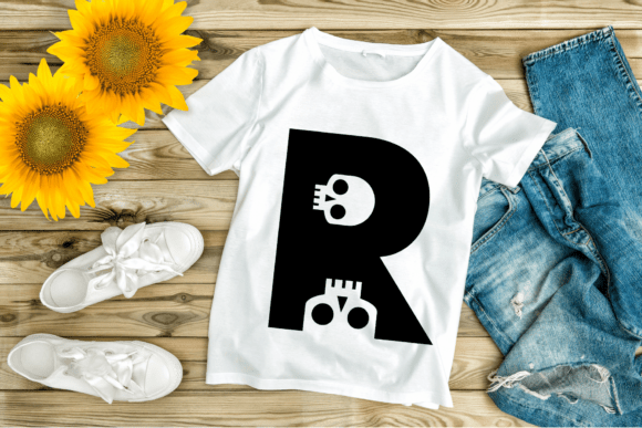 White t-shirt featuring a large black letter 'R' with skull design, laid on wooden surface with jeans and sunflowers.