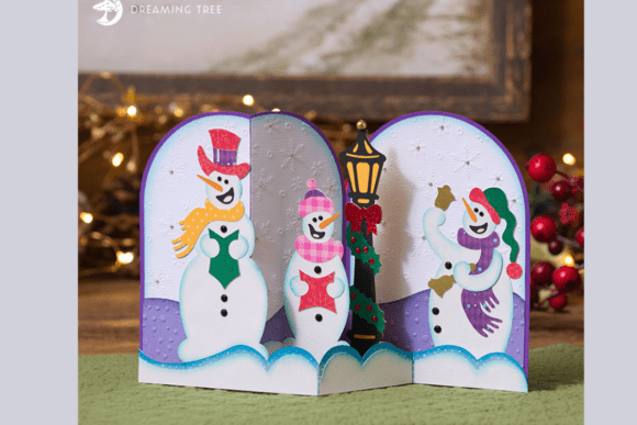 Open card showing three snowmen carolers, a lamppost, and a Christmas tree with a snowy background.