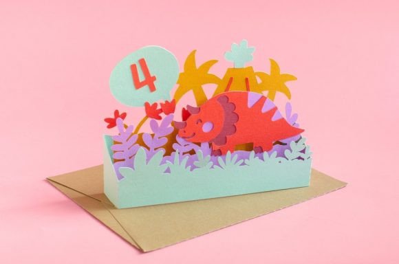 Pop-up card with a red triceratops, colorful plants, and a speech bubble with the number 4 on a pink background.