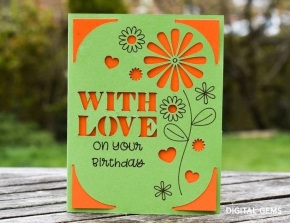 Green card with orange floral cutouts and 'WITH LOVE on your Birthday' text on a wooden surface.