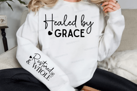 White sweatshirt featuring 'Healed by Grace' on front and 'Restored & Whole' on sleeve.