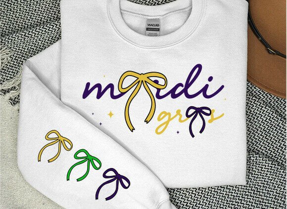 White sweatshirt with 'mardi gras' text and bow designs in purple, yellow, and green on sleeve.